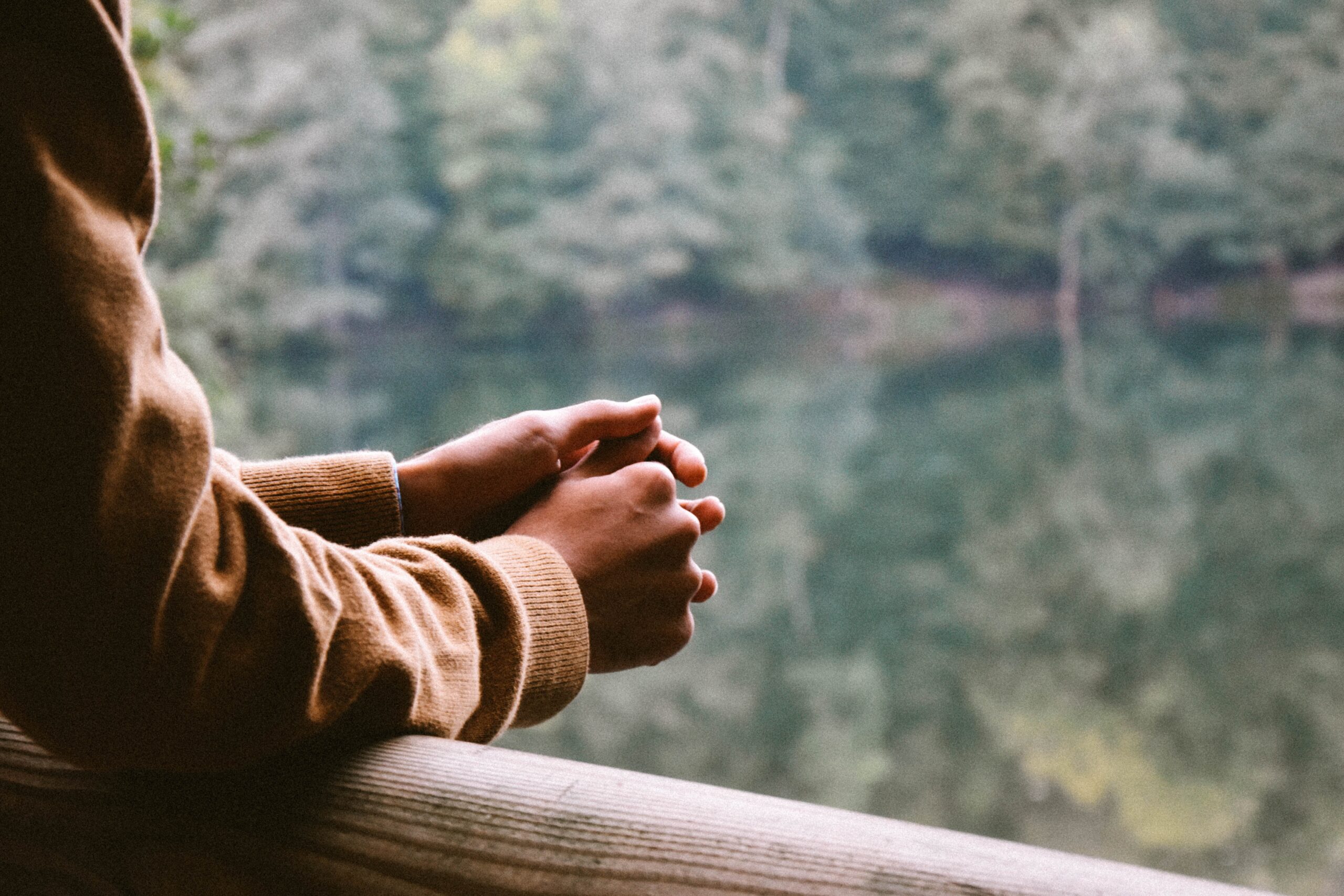 arms resting on a railing; person looking out on the water